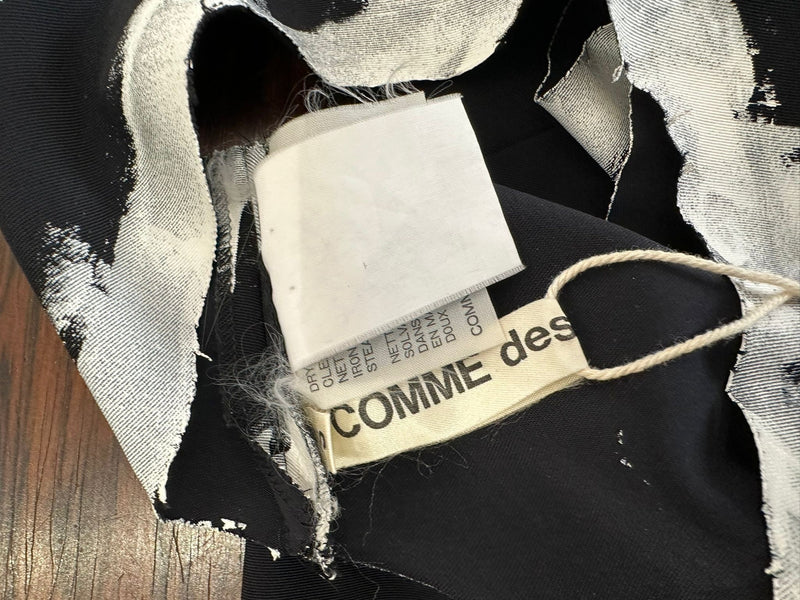 Flat lay of black asymmetrical dress by Comme des Garçons with hand-painted white border details